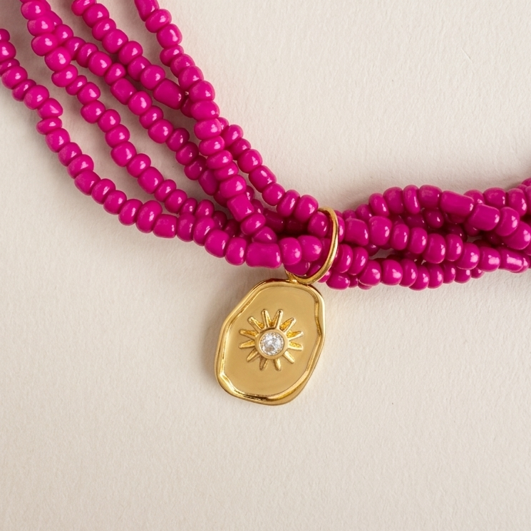 Pink beaded necklace with a gold pendant on a beige background