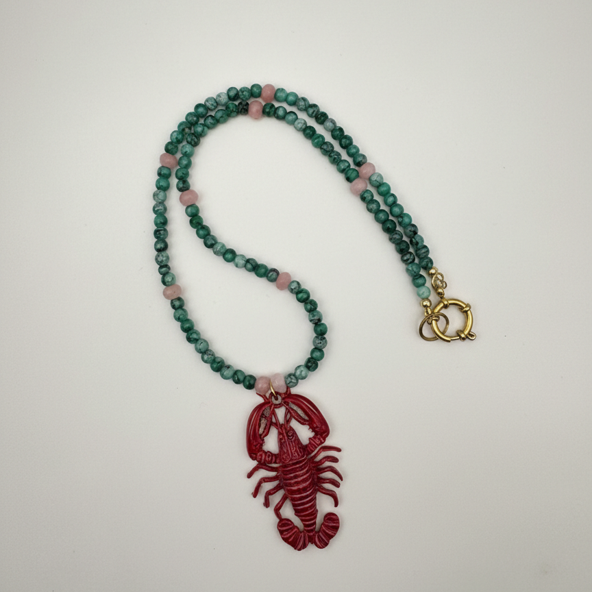 Handmade beaded necklace with green and purple beads and a pink lobster pendant_still