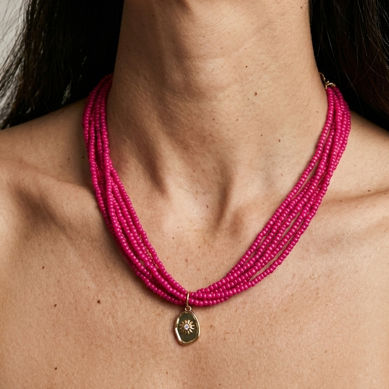 Close-up of a woman wearing a pink beaded necklace with a gold pendant.